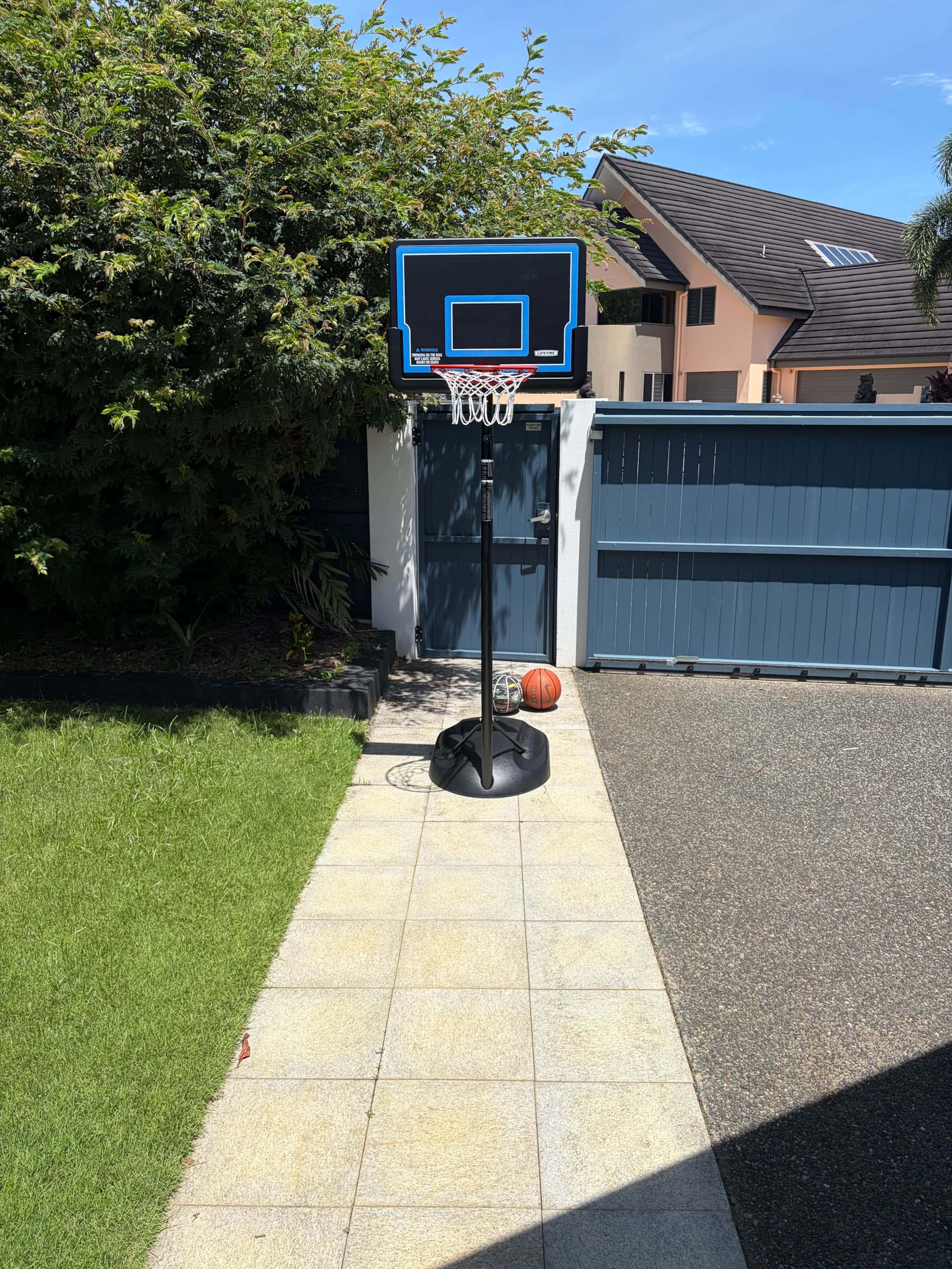 Portable basketball hoop with balls beside the driveway, ready to roll out to the cul-de-sac