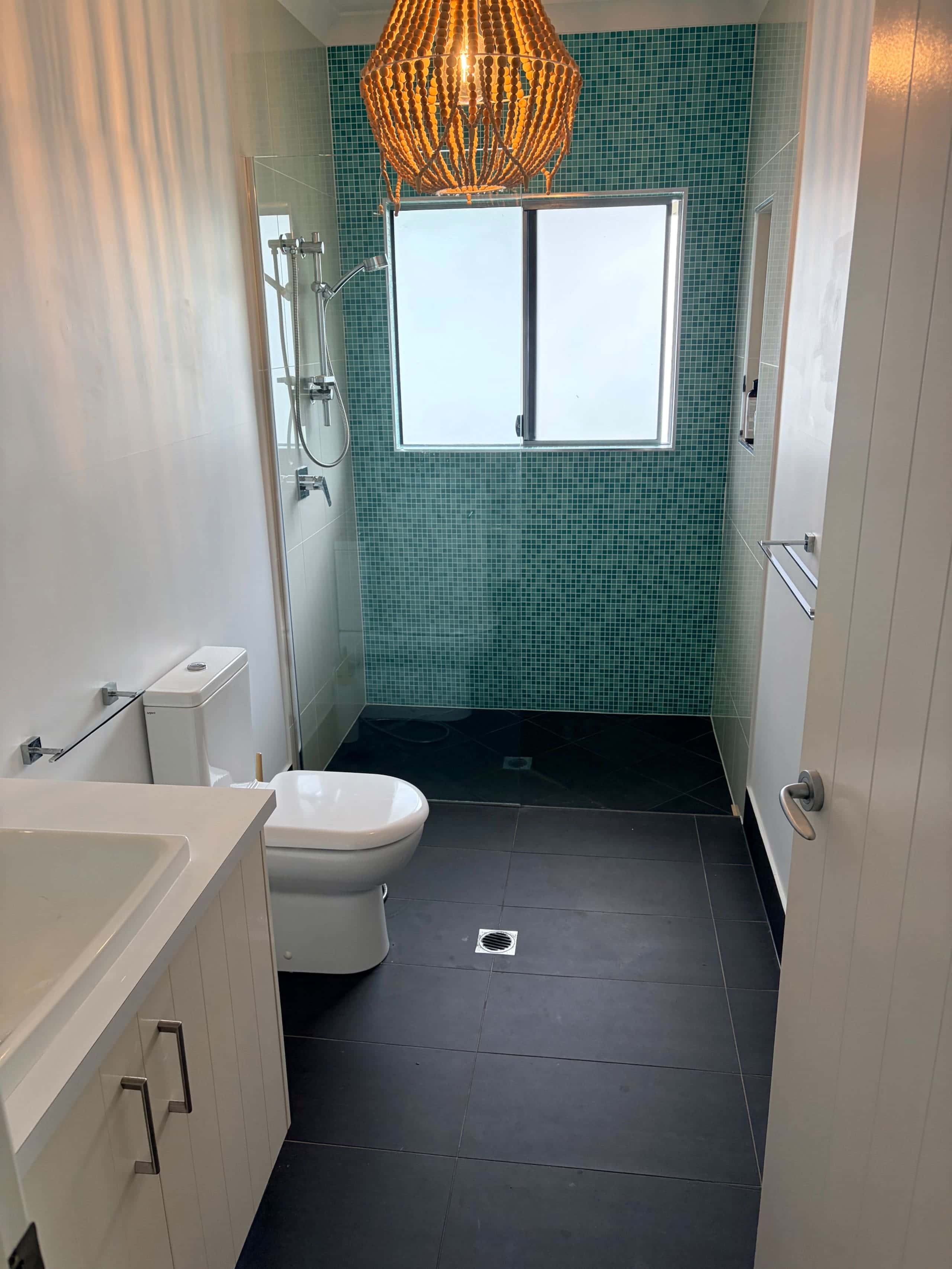 Bathroom with aqua mosaic shower wall, timber beaded pendant and stone-topped vanity