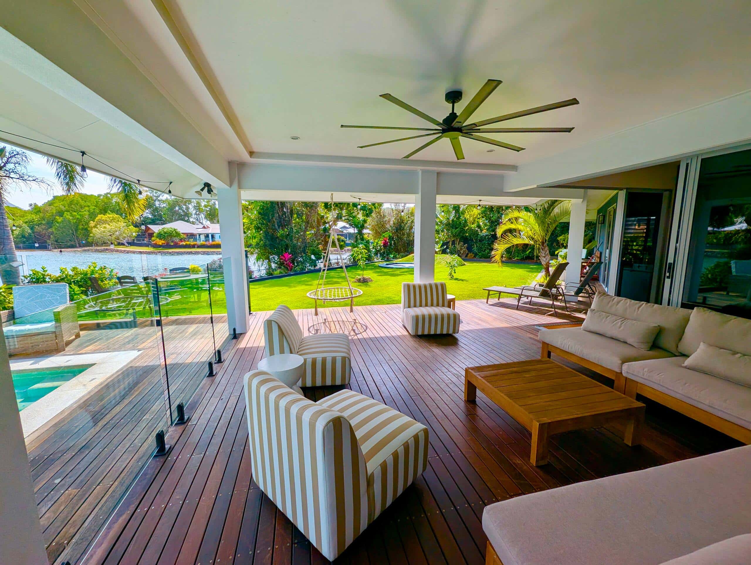 Covered outdoor lounge on the hardwood deck with striped armchairs, oversized ceiling fan and lagoon outlook