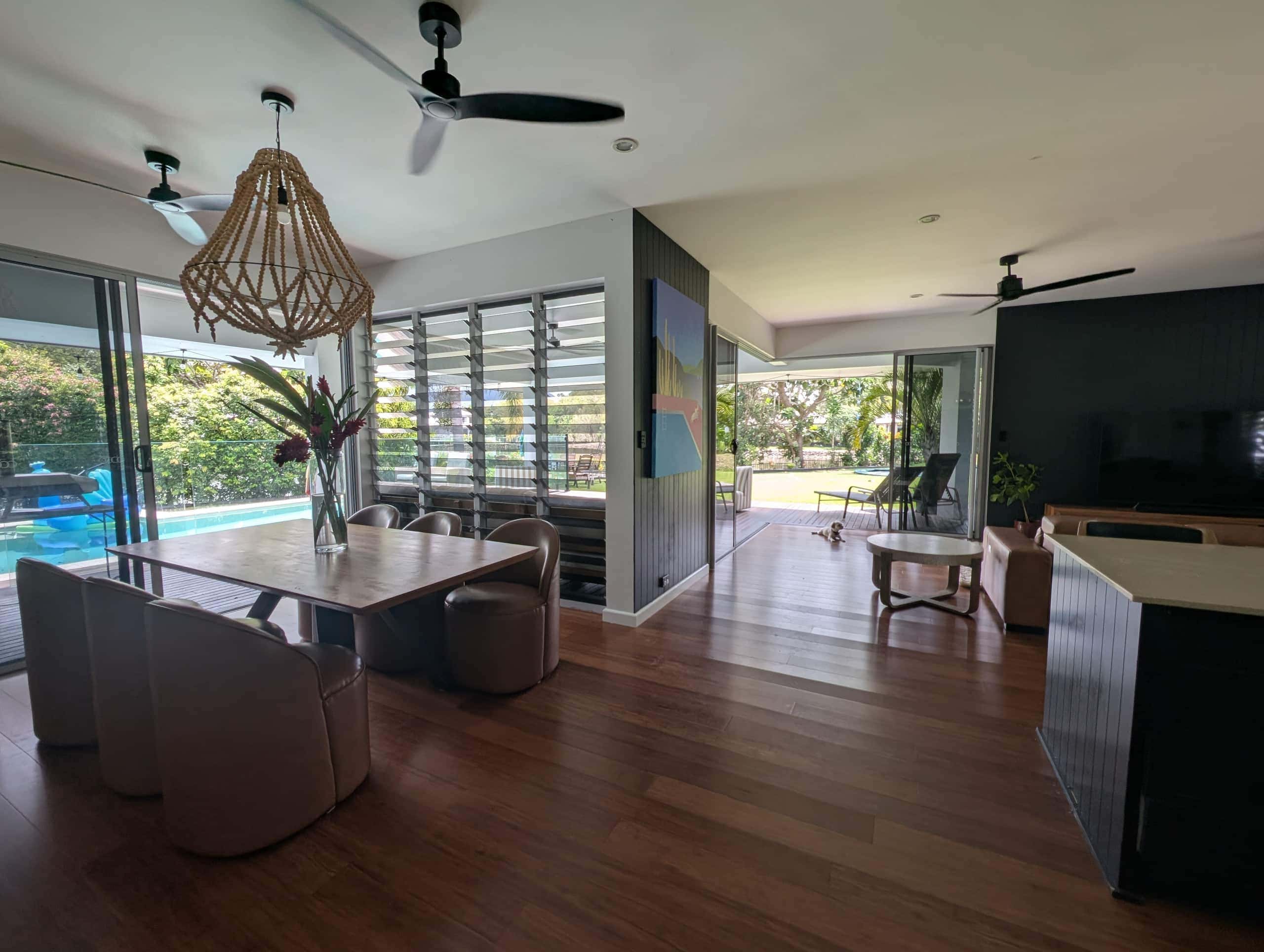 Dining table under a beaded pendant with louvre windows and sliding doors to the pool deck