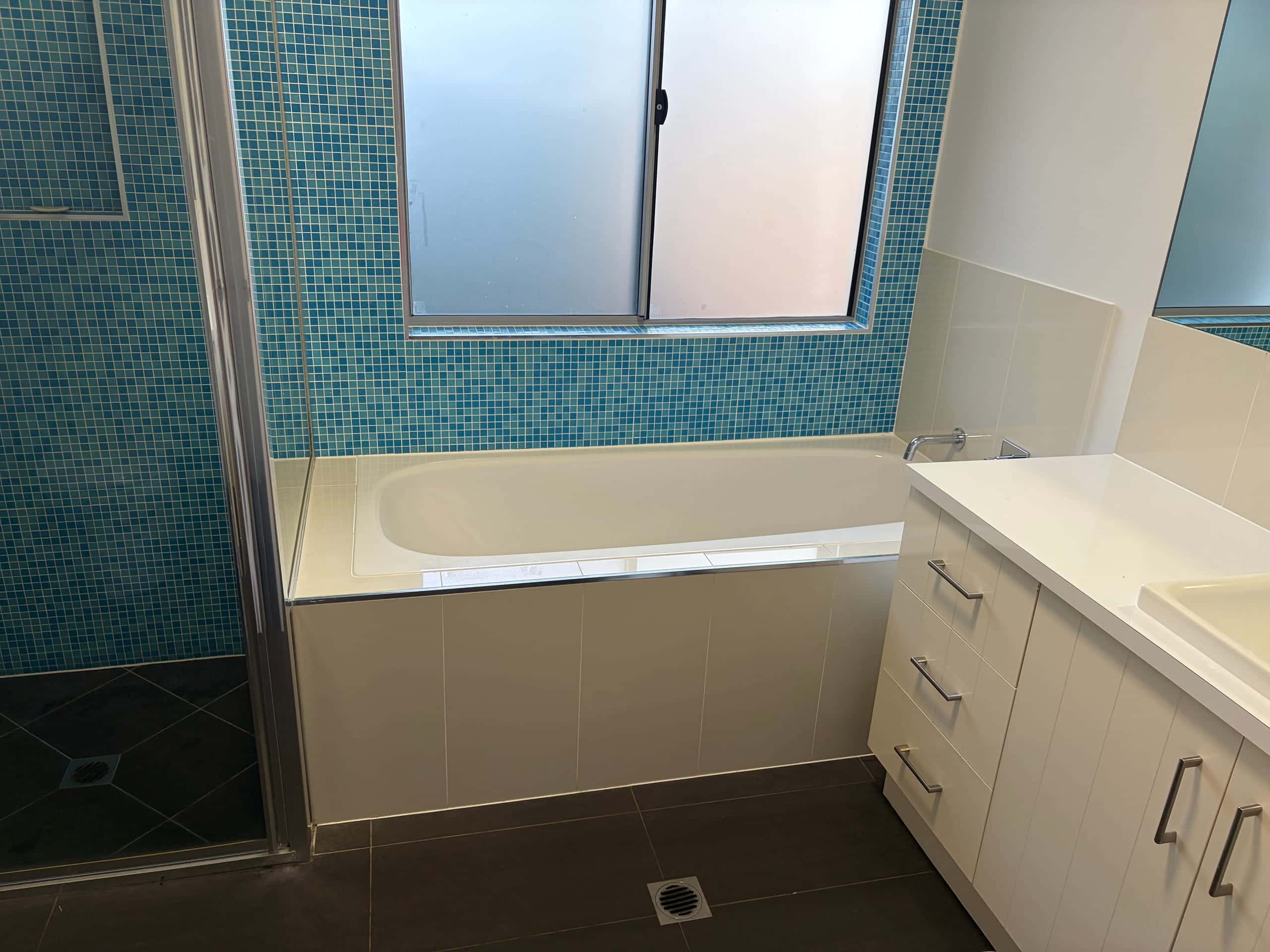 Family bathroom with full-size bathtub under a teal mosaic window wall and separate shower