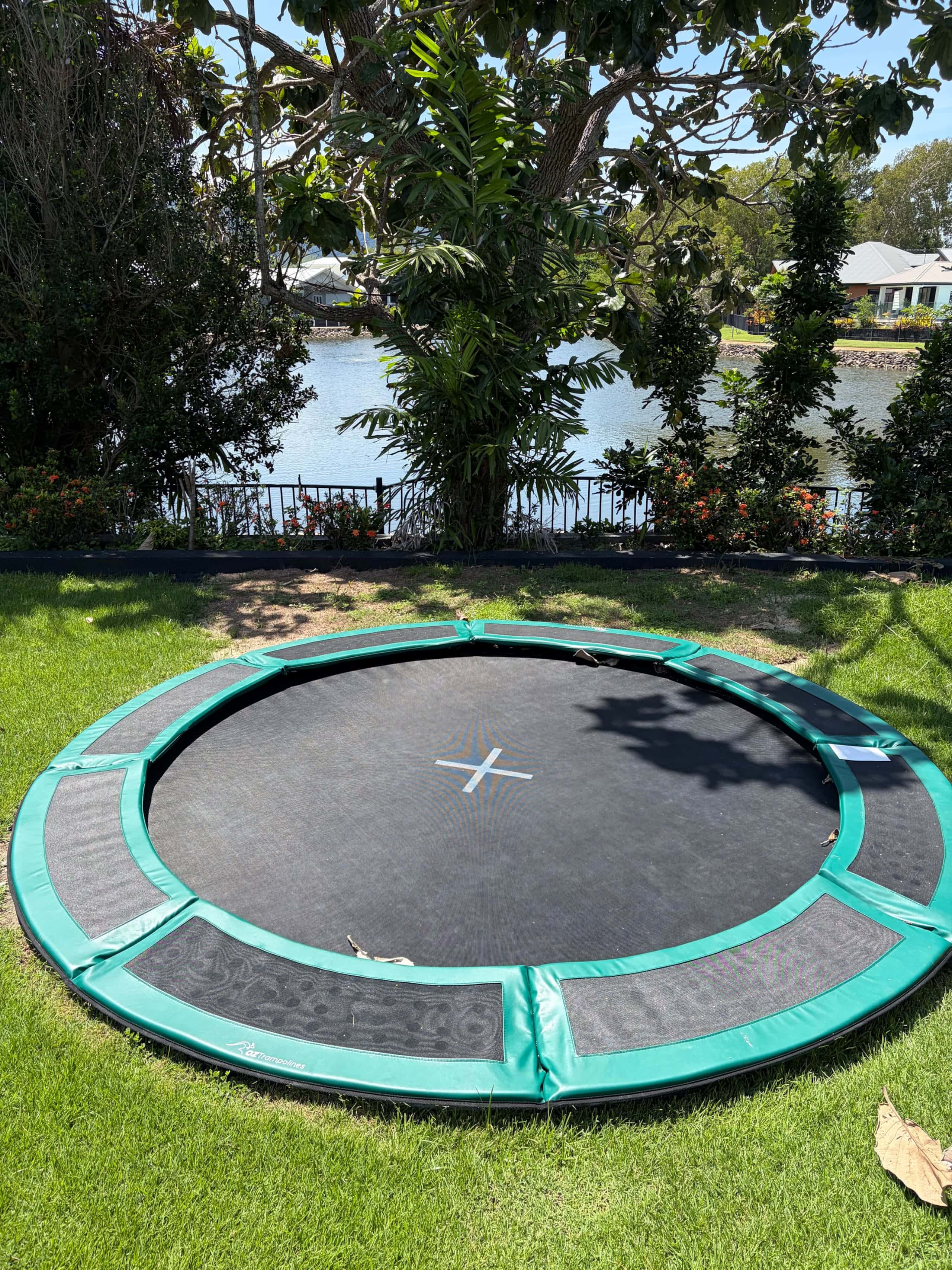 In-ground trampoline set flush into the lawn with the lagoon behind the garden fence