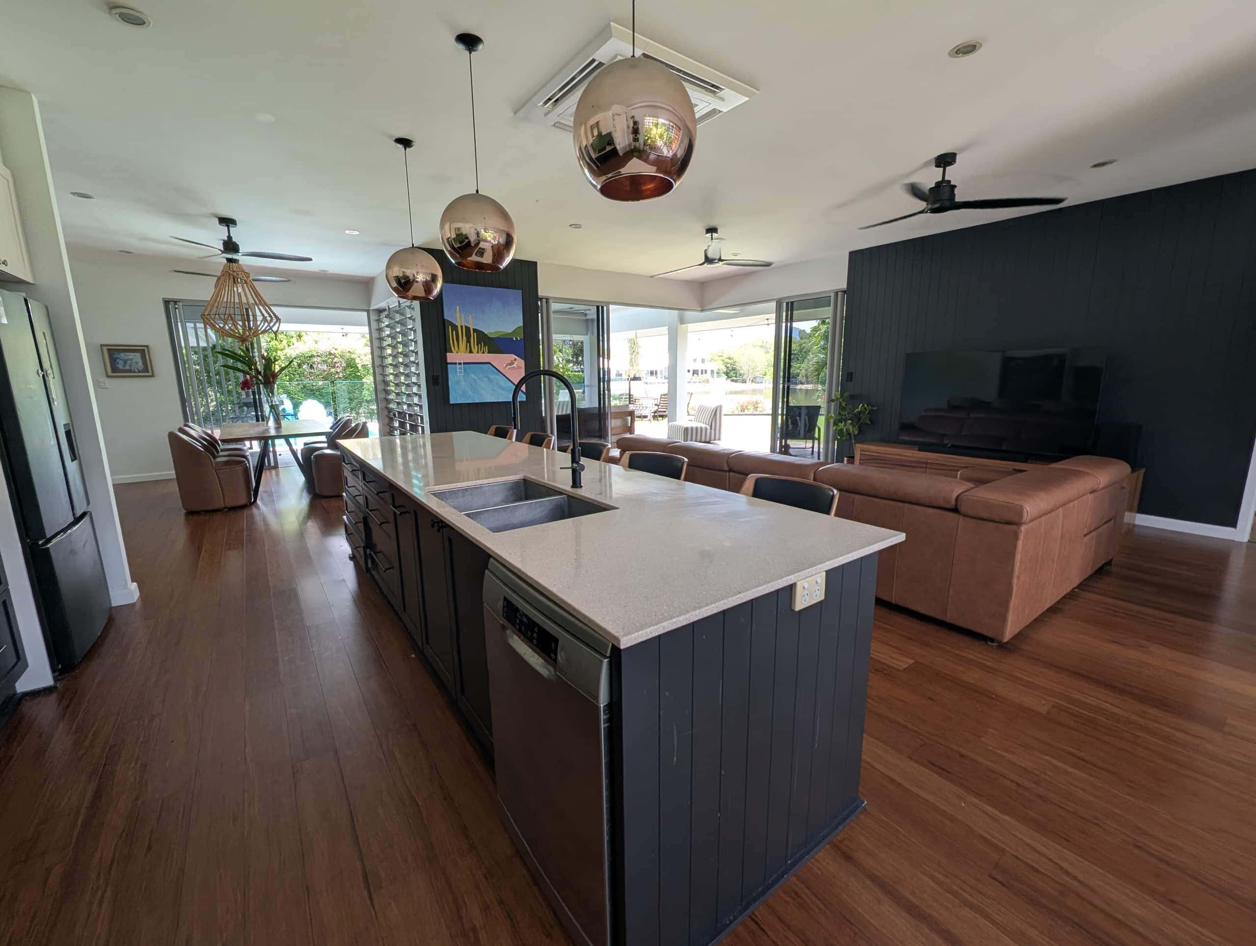 Stone-topped kitchen island with copper pendant lights looking through to the leather lounge and deck