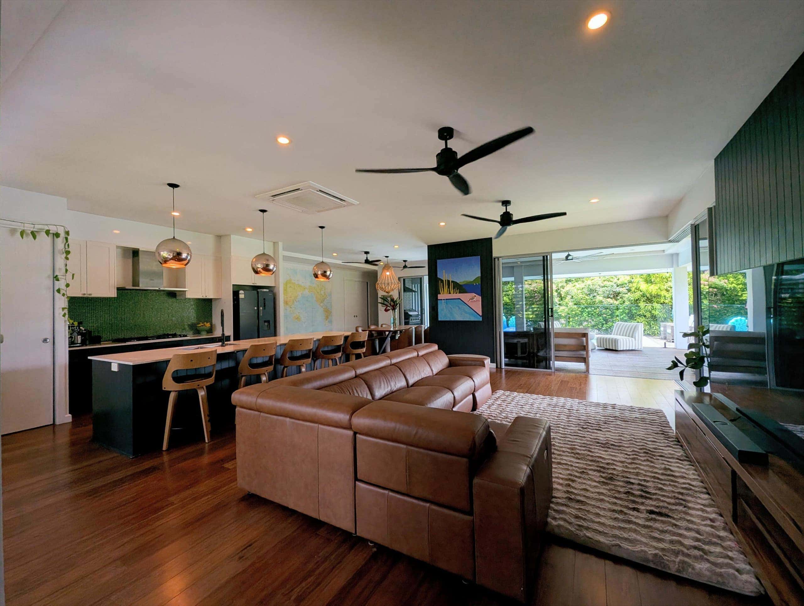 Open-plan living room with leather lounge, bamboo floors and green-tiled kitchen flowing to the deck