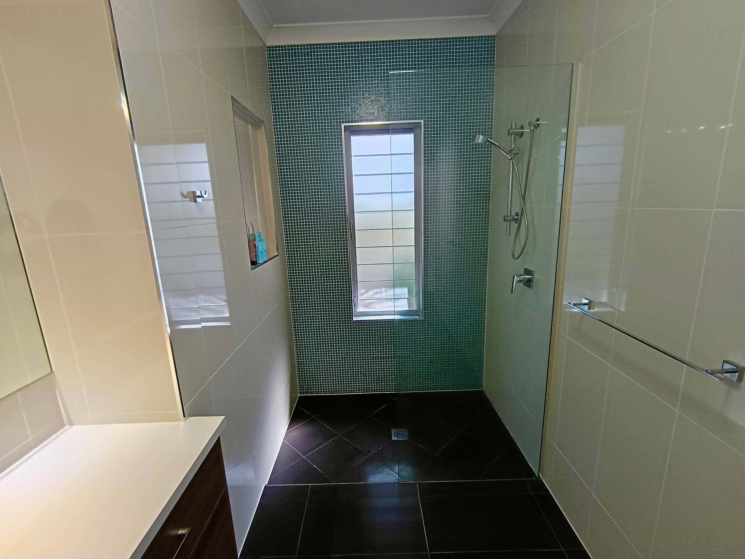 Walk-in shower with green mosaic feature wall, rain head and frameless glass