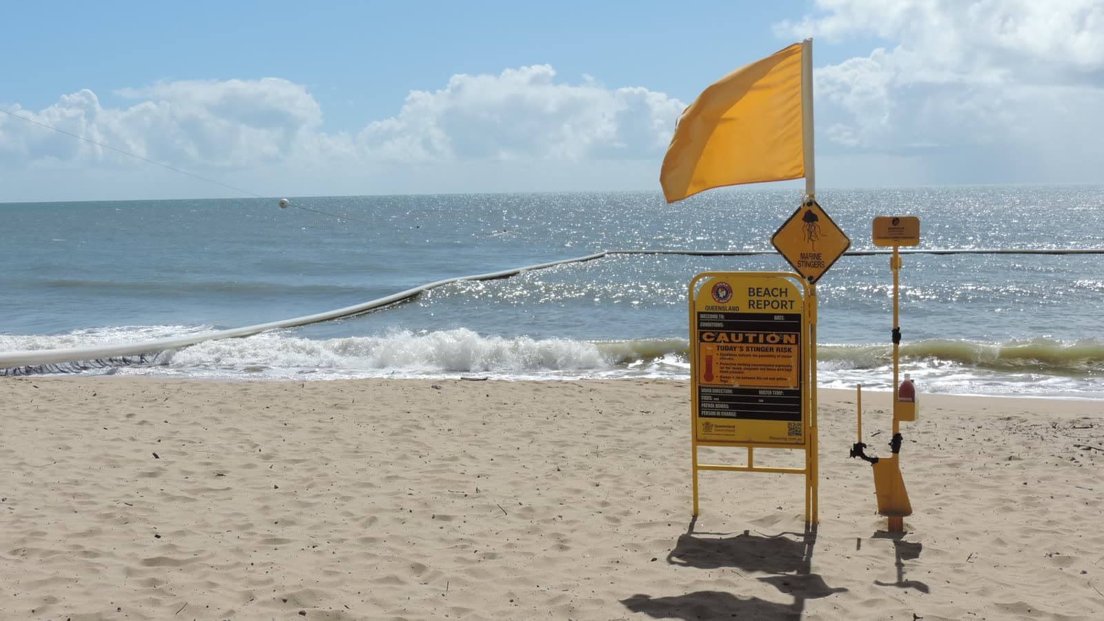 A marine stinger net strung across the shallows at Ellis Beach, beside the yellow beach report and stinger warning signs