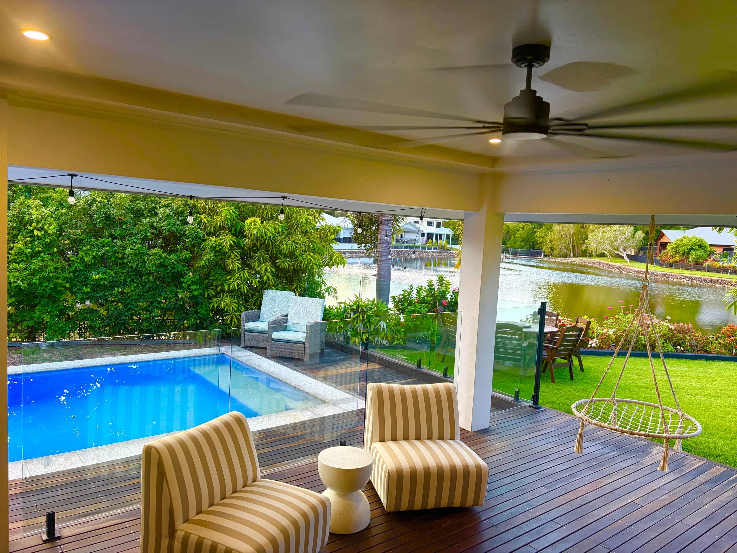 Deck corner with hanging swing chair beside the glass-fenced private pool and lagoon view