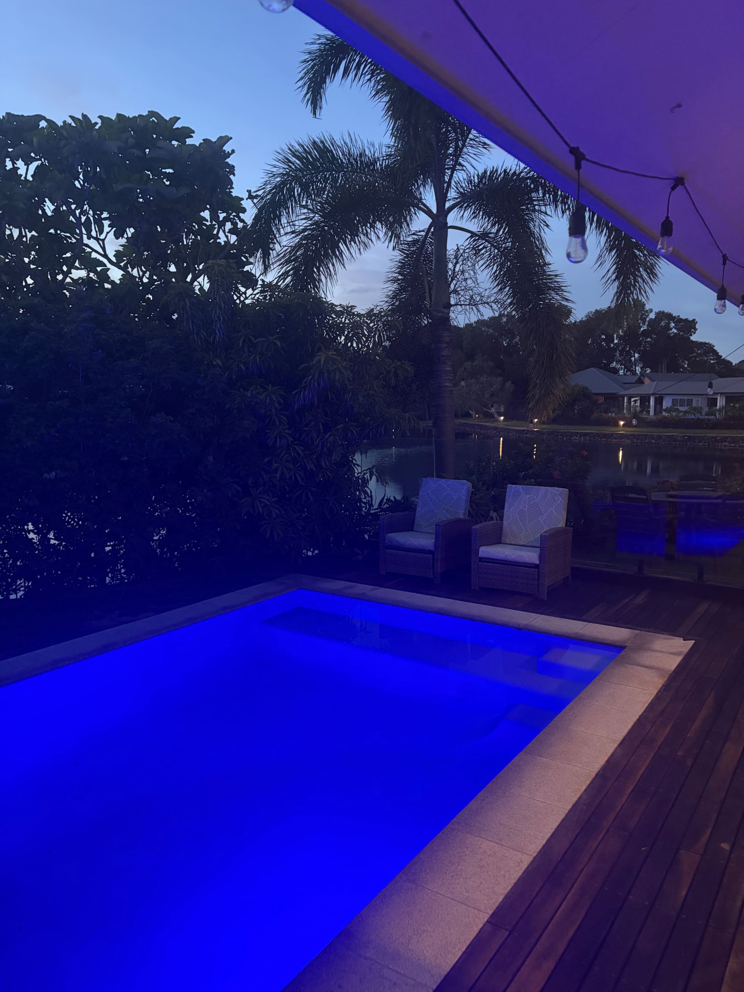 Private pool glowing blue at dusk under festoon lights with palm trees and the lagoon behind