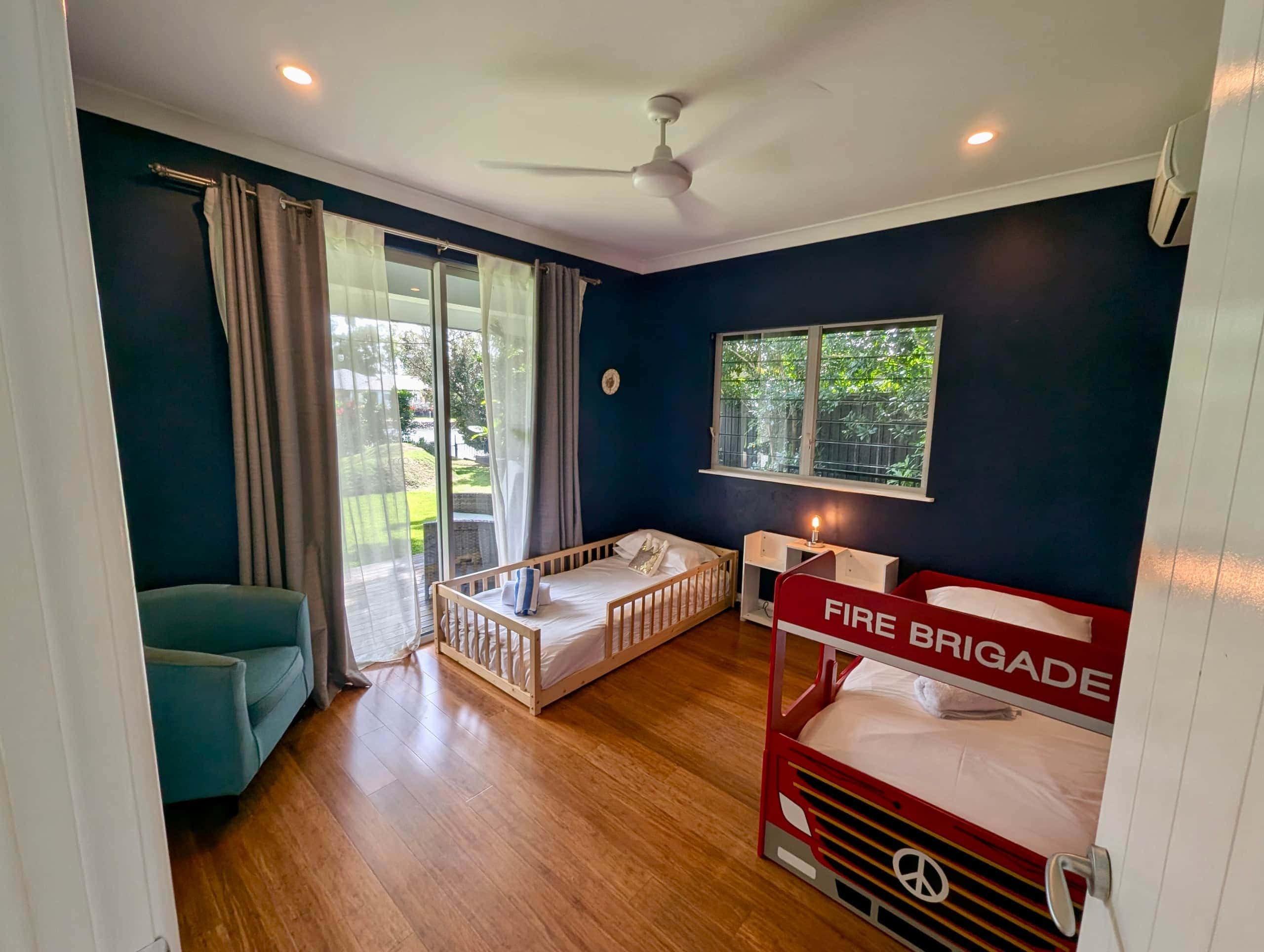 Kids bedroom with navy walls, fire-truck single bed and toddler floor bed opening to the garden