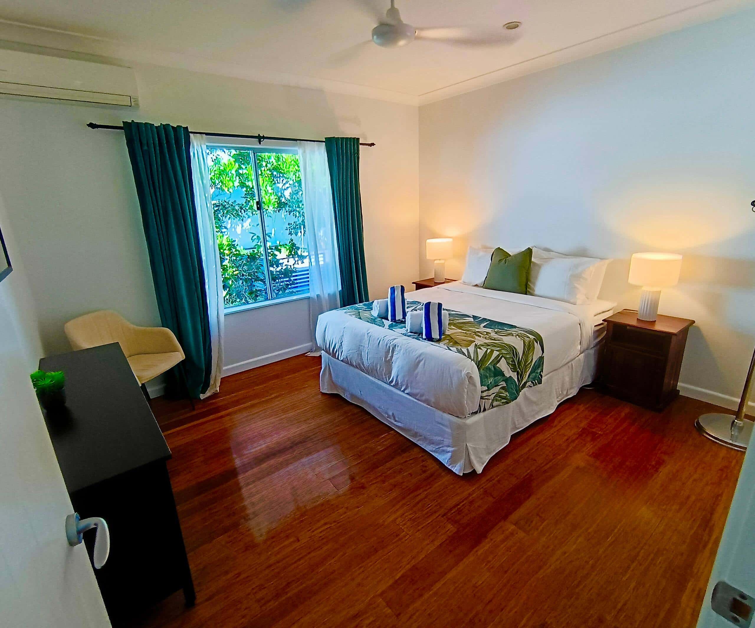 Queen bedroom with tropical-print quilt, deep green curtains, ceiling fan and air conditioning